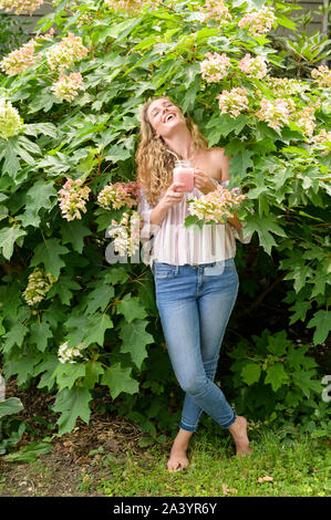 Sorridente giovane donna frullato di contenimento da fiori Foto Stock