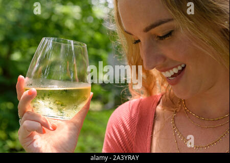 Sorridente giovane donna tenendo un bicchiere di vino bianco Foto Stock