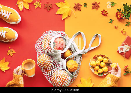 Autunno laici piatto su split rosso e arancione lo sfondo della carta. Orange zucche, mele e mele cotogne in maglia blu busta o sacchetto di stringa, giallo canvas sneakers, h Foto Stock