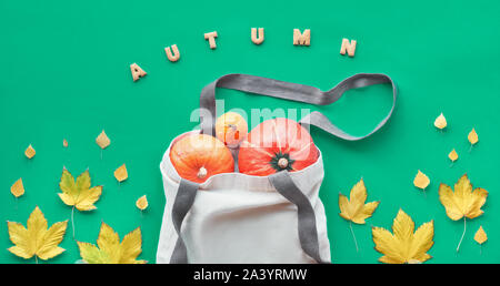 Autunno laici piatto su sfondo verde chiaro. Orange zucche, mele e mele cotogne in beige borsa in tela giallo e foglie di acero. Testo 'autunno' fatta da cooki Foto Stock