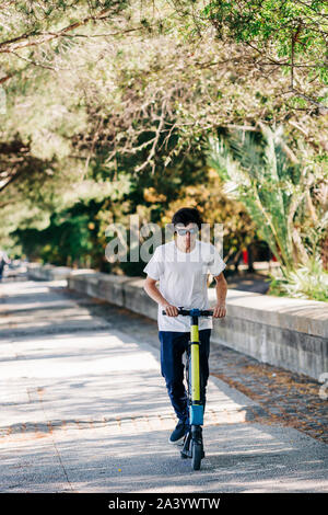 Giovane uomo utilizzando lo scooter elettrico sul marciapiede Foto Stock