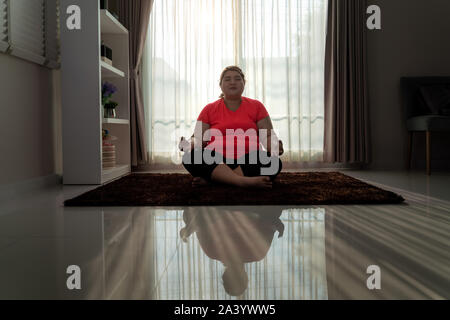 Asia Donna sovrappeso esercizio yoga posa facile da solo sul pavimento in casa, meditazione yoga esercizio a casa. Grasso donne prendersi cura della salute e si desidera Foto Stock