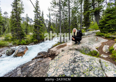 Donna matura accovacciato sulle rocce dal fiume a Stanley, Idaho, Stati Uniti d'America Foto Stock