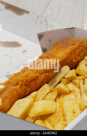 Pesce e patatine fritte in una scatola di cartone da asporto. Riciclaggio di imballaggi. Grigio sfondo di legno Foto Stock