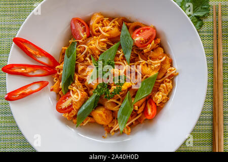 Tailandese tradizionale piatto a base di noodle Pad Thai con pollo serviti sul piatto di portata in ceramica bianca. Vista dall'alto. Bacchette sul lato. Sfondo verde. Foto Stock