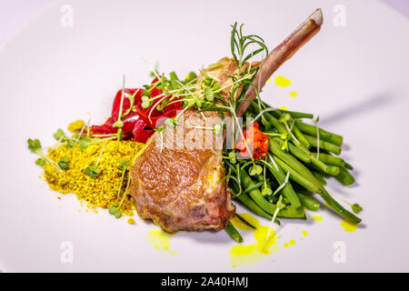 Bianco piastra in ceramica con un lamb chop, servita con saltata di fagioli verdi, cipolla colorata con succo di barbabietola, giallo trasportano pistacchio, con rosmarino e di essere Foto Stock