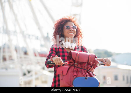 Ragazza indossando controllato shirt sorridente e bicicletta equitazione Foto Stock