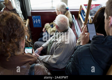 Due pendolari di utilizzare i loro telefoni cellulari al messaggio mentre sul bordo di una Londra-bound bus durante la mattina l'ora di punta, il 9 ottobre 2019, a Londra, in Inghilterra. Foto Stock