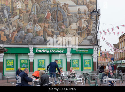 Un Paddy Power scommesse e uscita murale circa Dartford del patrimonio industriale da Gary Drostle su un angolo della campana in Kentish Town pedonalizzata High Street, il 3 ottobre 2019, in Dartford Kent, Inghilterra. Il murale è intitolata "Una città che ha cambiato il mondo" (2000) e celebra l'unico patrimonio industriale di Dartford nel Kent. Londra artista Gary Drostle è un premiato artista specializzato nella specifica per il sito arte, murales, il pavimento e la parete di mosaici e sculture a mosaico. Foto Stock