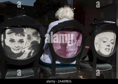 Una signora anziana seduto su una sedia dotata di film di Hollywood Stars Audrey Hepburn, James Dean e Marylin Monroe, attende il suo giro in un locale parrucchieri, il 2 ottobre 2019, in Sutton, Londra, Inghilterra. Gli elettori di Sutton votato 53,7% a favore di Brexit durante il referendum del 2016. Foto Stock