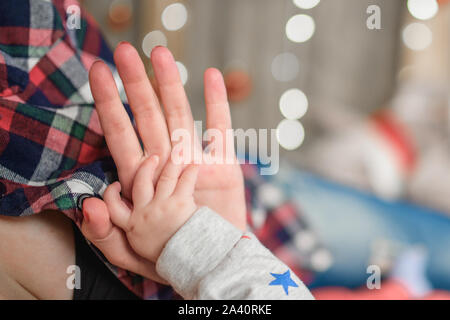 Baby la mano trattiene la madre la mano. contro lo sfondo di una defocalizzazione del nuovo anno di ghirlande. Natale piccolo miracolo. Anno nuovo, natale e capodanno Foto Stock