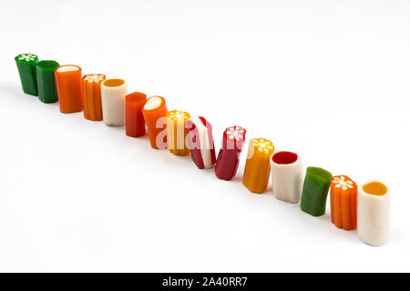 Una fila di caramelle colorate di varie forme su una superficie bianca Foto Stock