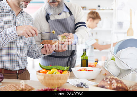 Close-up del giovane uomo in piedi e salsa di degustazione dando dall'uomo maturo durante la loro preparazione in cucina il cibo Foto Stock