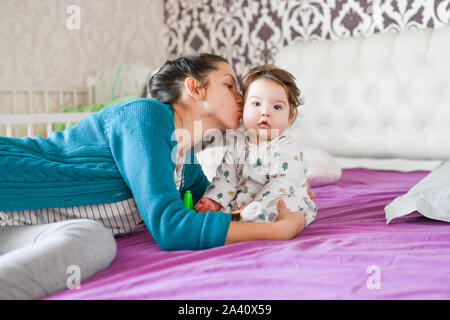 Mom e amore per il bambino sul letto. le emozioni di felicità. kissing baby e avvolgente. Pretty Woman tenendo un neonato nelle sue braccia Foto Stock