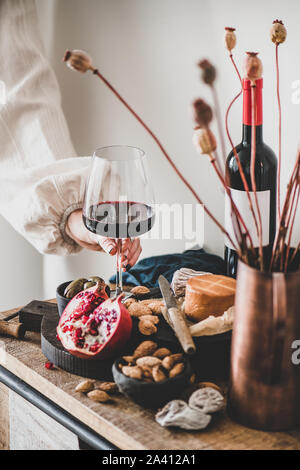 Womans mano che tiene un bicchiere di vino rosso su vari snack Foto Stock