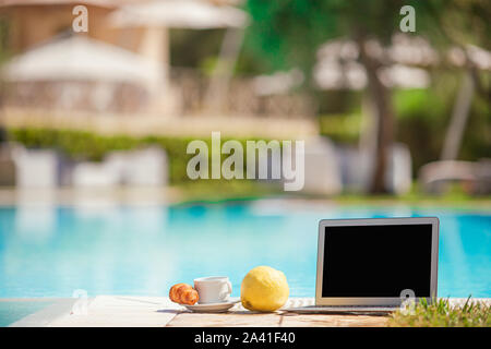 Colazione deliziosa e un computer portatile sul bordo della piscina esterna Foto Stock