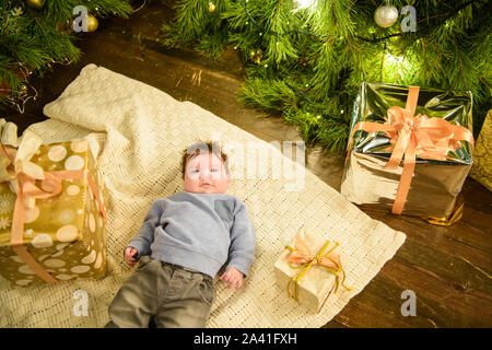 Bambino vicino albero di natale vista dall'alto. Closeup ritratto di sorridere grazioso fanciullo in vacanza interni di natale vicino alla struttura di festa. Vista dall'alto di felice Foto Stock