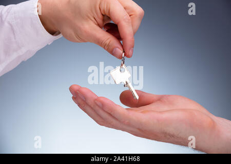 Close-up di Agente Immobiliare Mano che dà le chiavi al proprietario contro uno sfondo grigio Foto Stock