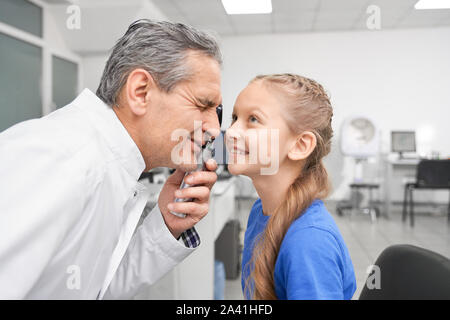 Vista laterale della ragazza sorridente largamente apertura occhi mentre maschio controllo medico oculista gli occhi con l'attrezzo speciale. Il sambuco esperto medico visione di test in clinica. Concetto di correzione della vista e oftalmologia. Foto Stock