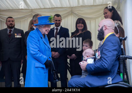 Queen Elizabeth II soddisfa con il veterano Dan Phillips e suo figlio Harry (indossare tuta blu e Cravatta gialla) come ella visite Haig alloggiamento fiducia, Morden, Londra Sud, ad aprire ufficialmente il loro nuovo sviluppo di alloggiamento per le forze armate di veterani e l'ex-community del servizio. Foto Stock