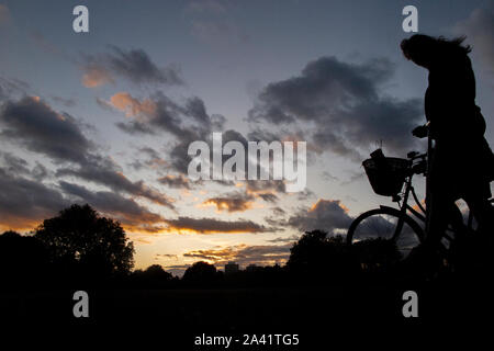 Un ciclista passeggiate home sotto un tempestoso tramonto in un parco di Londra Foto Stock