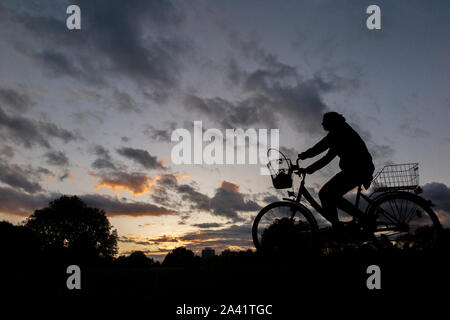 Un ciclista rides home sotto un tempestoso tramonto in un parco di Londra Foto Stock