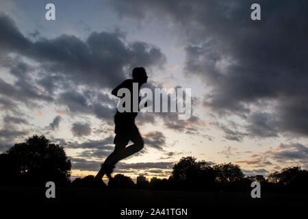 Un ciclista rides home sotto un tempestoso tramonto in un parco di Londra Foto Stock