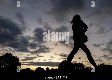Una singola ragazza cammina home sotto un tempestoso tramonto in un parco di Londra Foto Stock