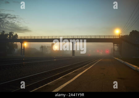 Stazione ferroviaria di notte nella nebbia è illuminato da lampioncini giallo a distanza Foto Stock