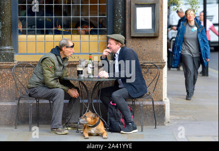 Londra, Regno Unito. Due uomini e un cane fuori il Clarence pub di Whitehall. Uno di bere birra, l'altro vino Foto Stock