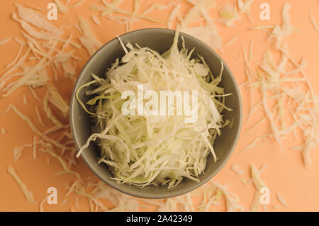 Tritate finemente il cavolo bianco su sfondo beige,cavolo nella ciotola e intorno sulla superficie,cavolo tagliato in stile minimalista,verdure rustico Foto Stock