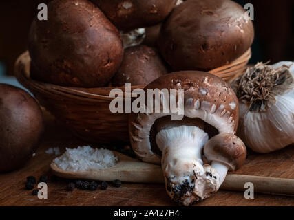 Marrone a Parigi o funghi champignon proveniente da un contenitore di colore rosso su una tavola di legno con un cucchiaio di legno e sale. Foto Stock