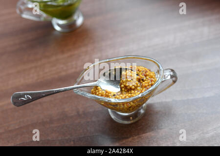 La senape in una ciotola di vetro. Grano francese la senape in una ciotola. Grano francese la senape in una ciotola di vetro bianco sul tavolo di legno Foto Stock