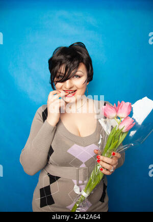 Bella ragazza nel carino maglione con fiori tulipani in mani su uno sfondo blu da soli Foto Stock