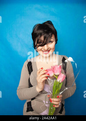Bella ragazza nel carino maglione con fiori tulipani in mani su uno sfondo blu da soli Foto Stock