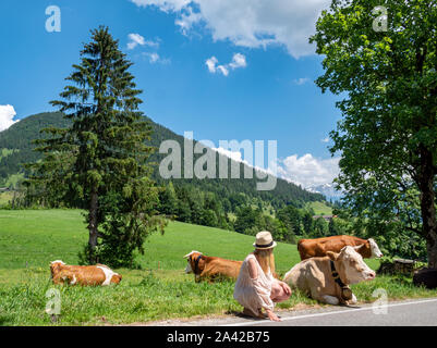 Donna con le vacche da latte in un pascolo di montagna nelle Alpi Foto Stock