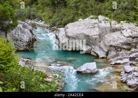 Fiume turchese Soca che scorre tra grandi rocce calcaree e attraverso una lussureggiante foresta verde vicino a Kobarid nelle Alpi Giulie, Slovenia. Foto Stock