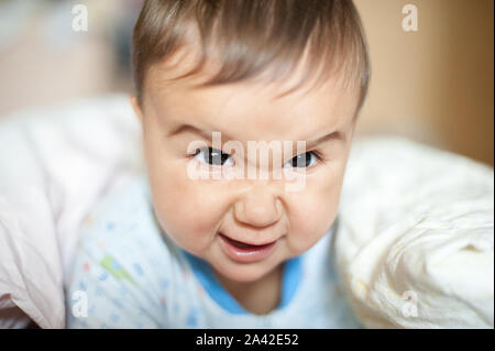 Ritratto di bimbo arrabbiato, furioso, accigliata e agressive giacente su una coperta. Divertente faccia del neonato Foto Stock
