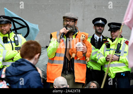 Un attivista ambientale con una bambola parla durante la dimostrazione.estinzione ribellione attivisti ambientali raccolte al di fuori della BBC a Londra per aumentare la consapevolezza dell'ecologica e crisi climatica e di esigere la copertura effettiva del crisi ambientale. Foto Stock