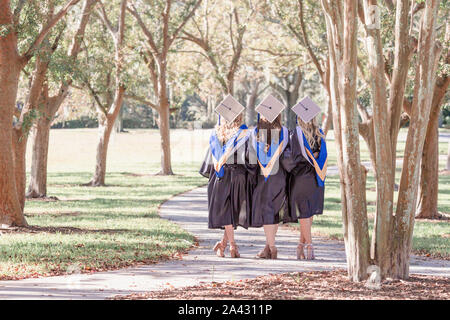 Tre amici in tappi di graduazione e gli abiti sui bracci del percorso intorno alla vita Foto Stock