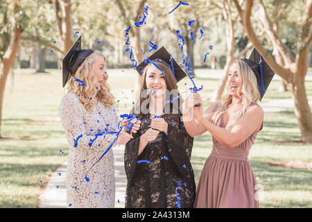 Tre donne caucasiche in tappi di graduazione di ridere e di popping coriandoli Foto Stock