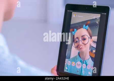 Donna che utilizza Snapchat multimedia messaging app con maschera facciale su tablet Foto Stock