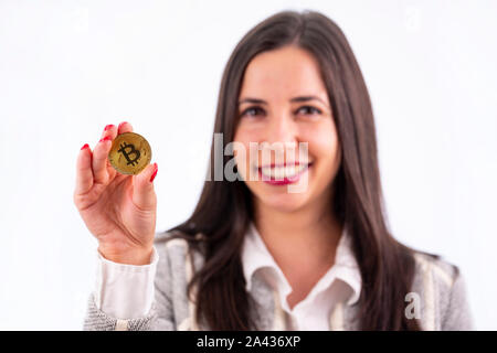 Virtual cryptocurrency denaro Bitcoin medaglia d'oro nella mano destra di una donna con il rosso smalto per unghie. Bellissimo modello femminile sorridente. Il futuro di mone Foto Stock