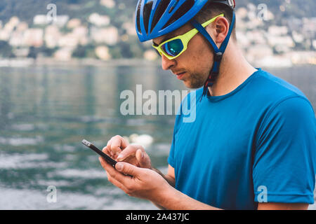 Il tema del turismo e dei viaggi in Italia. Un maschio ciclista utilizza un telefono sulla riva del lago di Como. Guy turistica in un casco con una bicicletta sulla riva Foto Stock