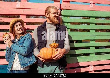 Halloween Preparaton concetto. Coppia giovane in piedi isolato sulla staccionata in legno con diverse varietà di zucche cercando riposo giocoso Foto Stock