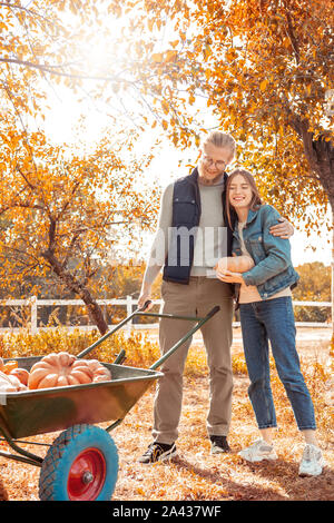 Halloween Preparaton concetto. Coppia giovane permanente al giardino con zucche guardando carrello pieno di raccolto gioioso sorridente Foto Stock