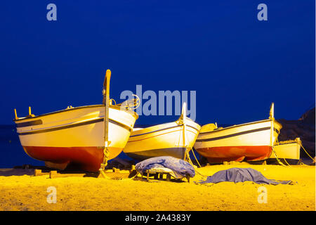 Tre barche da pesca su di una spiaggia di sabbia in serata contro lo sfondo del mare. La luce delle lanterne, riva del mare nella città spagnola di Tossa d Foto Stock