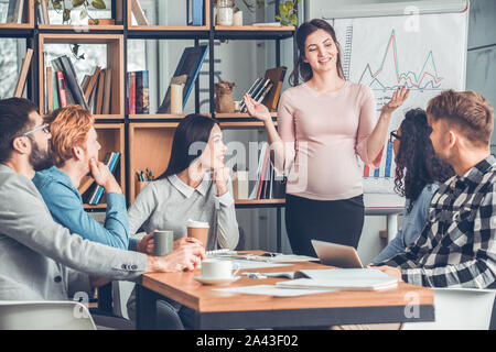 Startupers lavorando insieme a Office seduta guardando la donna incinta in piedi sharin idee per avvio felice Foto Stock