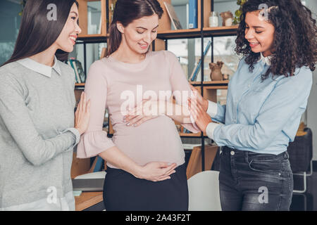 Startupers femmina lavorando insieme a Office in piedi che guarda alla pancia del collega incinta allegro Foto Stock
