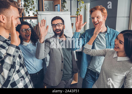 Startupers lavorando in ufficio insieme in piedi dando alta cinque allegro Foto Stock